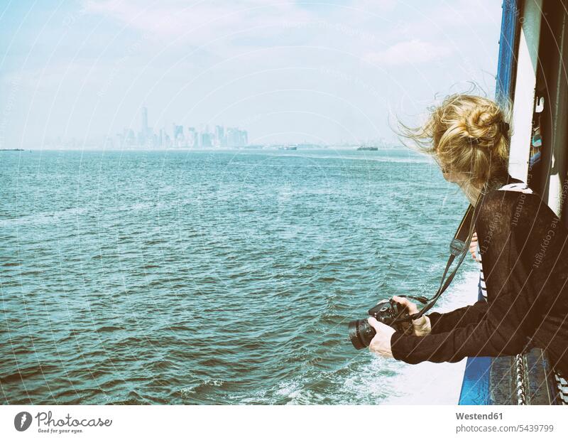 USA, New York City, Tourist mit Kamera auf der Staten Island Ferry mit Blick auf die Skyline von Manhattan und den East River Europäer Kaukasier kaukasisch