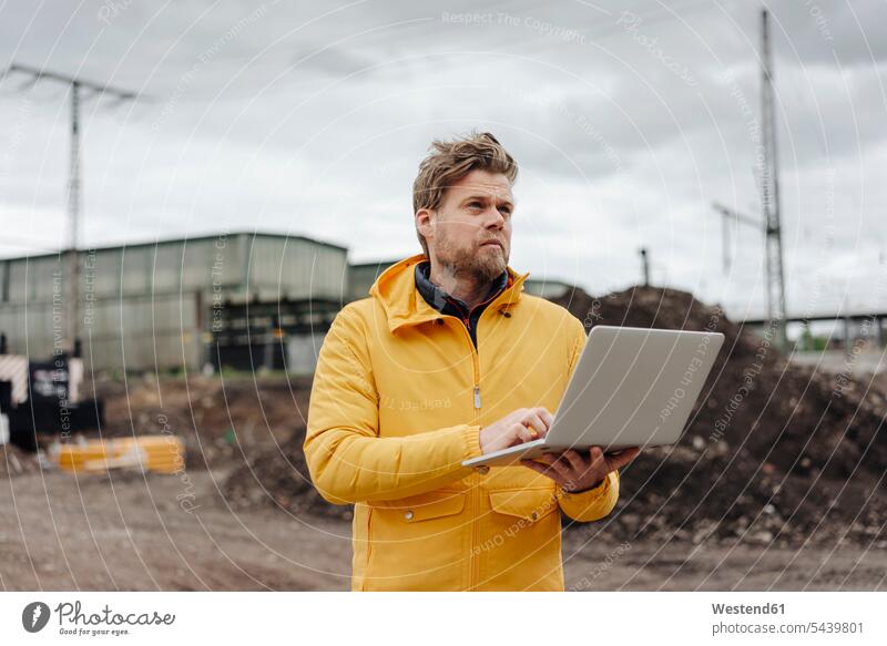 Mann mit Laptop in der Hand, im Hintergrund die Baustelle Kompetenz kompetent Ingenieur Ingenieure Arbeit Job Notebook Laptops Notebooks arbeiten prüfen