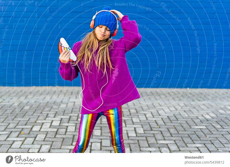 Porträt von Mädchen tanzen im Freien beim Hören von Musik mit Kopfhörern und Smartphone Spanien iPhone Smartphones modisch Kindheit Wollmütze Wollmützen