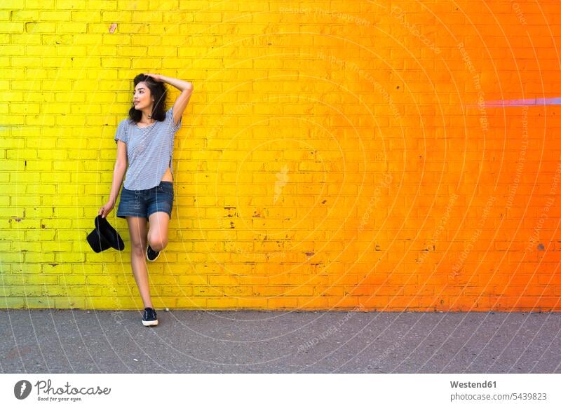 Junge Frau lehnt an gelber Ziegelmauer Lateinamerikaner Lateinamerikanisch Hispanier Latinos auf einem Bein Portrait Porträt Portraet Portraets Porträts