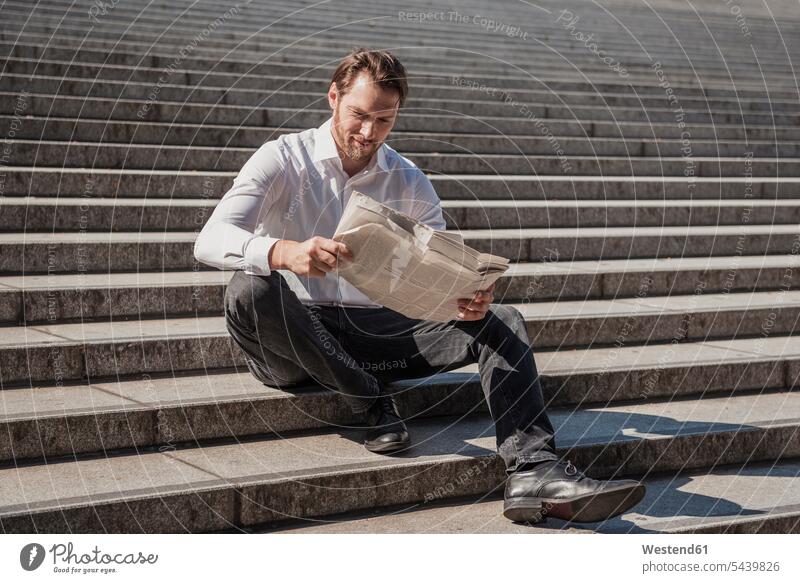 Lächelnder Geschäftsmann sitzt auf einer Treppe und liest Zeitung sitzen sitzend lesen Lektüre Businessmann Businessmänner Geschäftsmänner Treppenaufgang