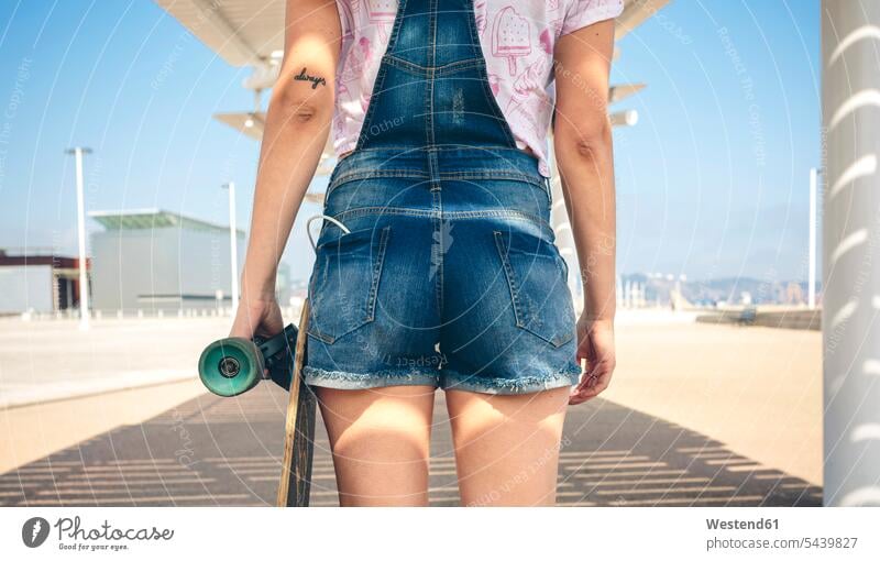 Rückenansicht einer jungen Frau mit Longboard an der Strandpromenade, Teilansicht Skateboarderin Skateboardfahrerin Skaterin Skateboarderinnen Skaterinnen