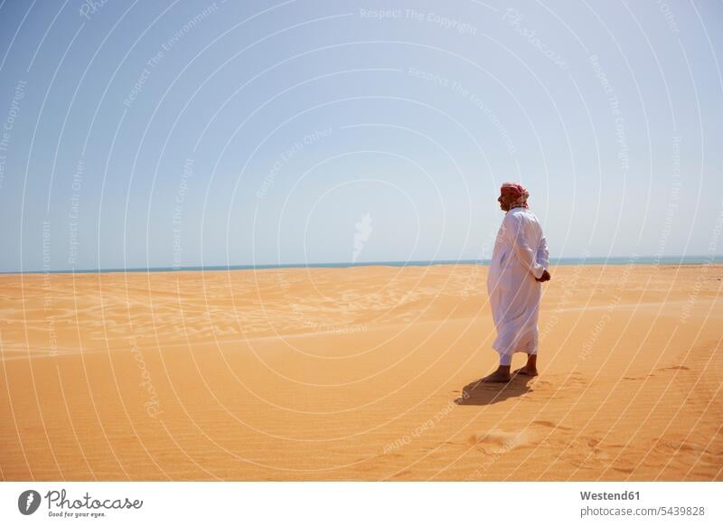 Beduine in Nationaltracht in der Wüste stehend, Rückansicht, Wahiba Sands, Oman Kopftücher Erwartung sehnsüchtig Streben steht frei auf Achse in Bewegung sandig
