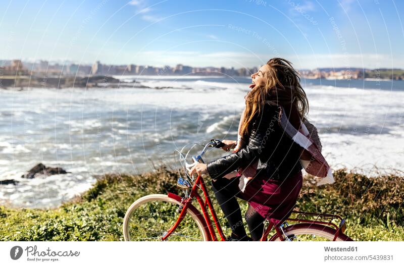 Spanien, Gijon, verspielte junge Frau beim Fahrradfahren an der Küste Europäer Kaukasier Europäisch kaukasisch Himmel Unbeschwert Sorglos Bikes Fahrräder Räder