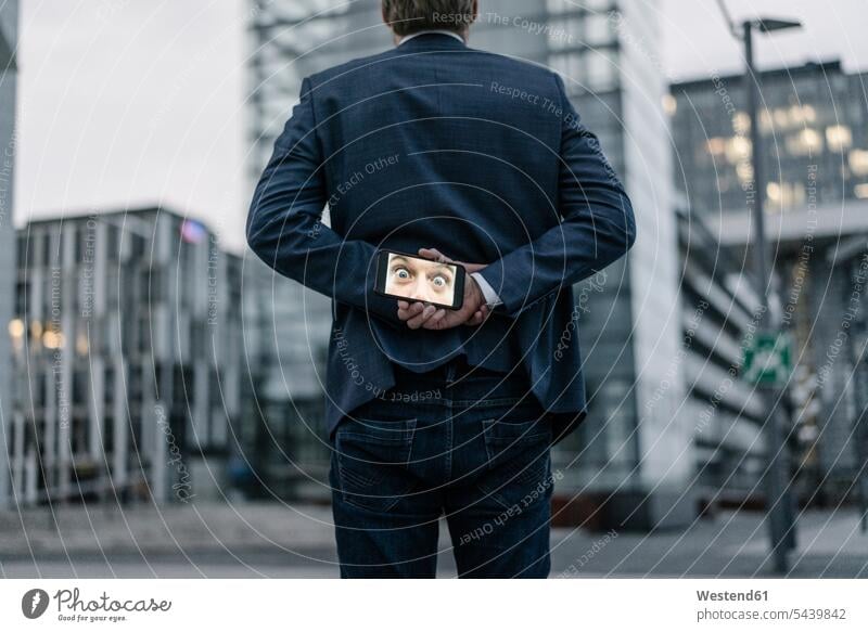 Geschäftsmann hält Mobiltelefon mit dem Bild der Augen hinter seinem Rücken halten Foto Fotos Businessmann Businessmänner Geschäftsmänner Menschliche Augen