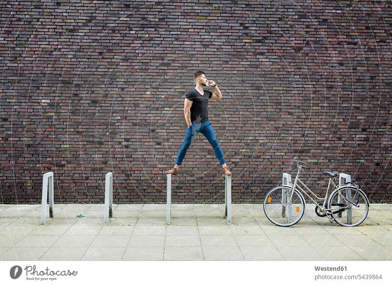 Mann mit Handy balanciert auf Fahrradträger vor Ziegelmauer ernst Ernst Ernsthaftigkeit ernsthaft Ziegelwand Backsteinmauer stehen stehend steht Männer männlich