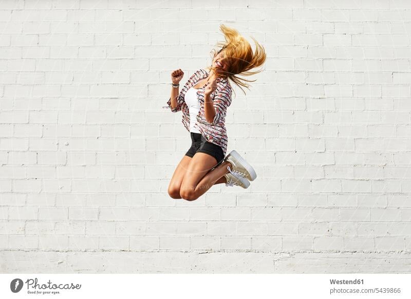 Glückliche junge Frau springt in der Luft vor einer weißen Wand weiblich Frauen springen hüpfen Spaß Spass Späße spassig Spässe spaßig glücklich glücklich sein