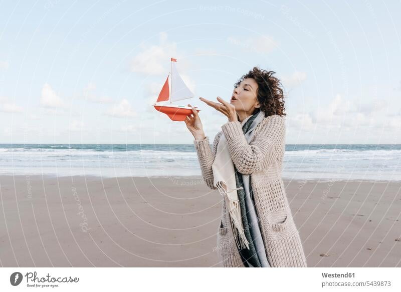 Frau bläst auf Spielzeugboot am Strand Portrait Porträts Portraits weiblich Frauen Beach Straende Strände Beaches pusten blasen Erwachsener erwachsen Mensch