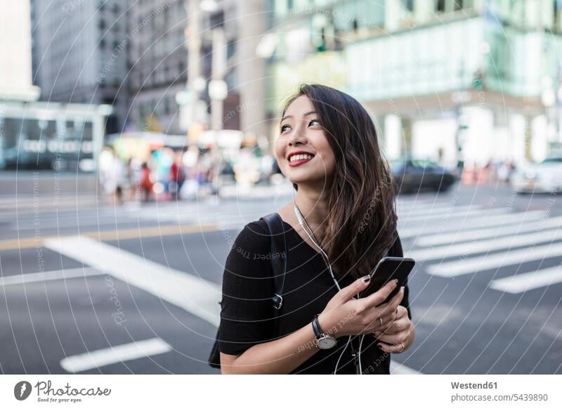 USA, New York City, Manhattan, junge Frau, die auf der Straße mit Handy und Kopfhörern Musik hört weiblich Frauen Erwachsener erwachsen Mensch Menschen Leute