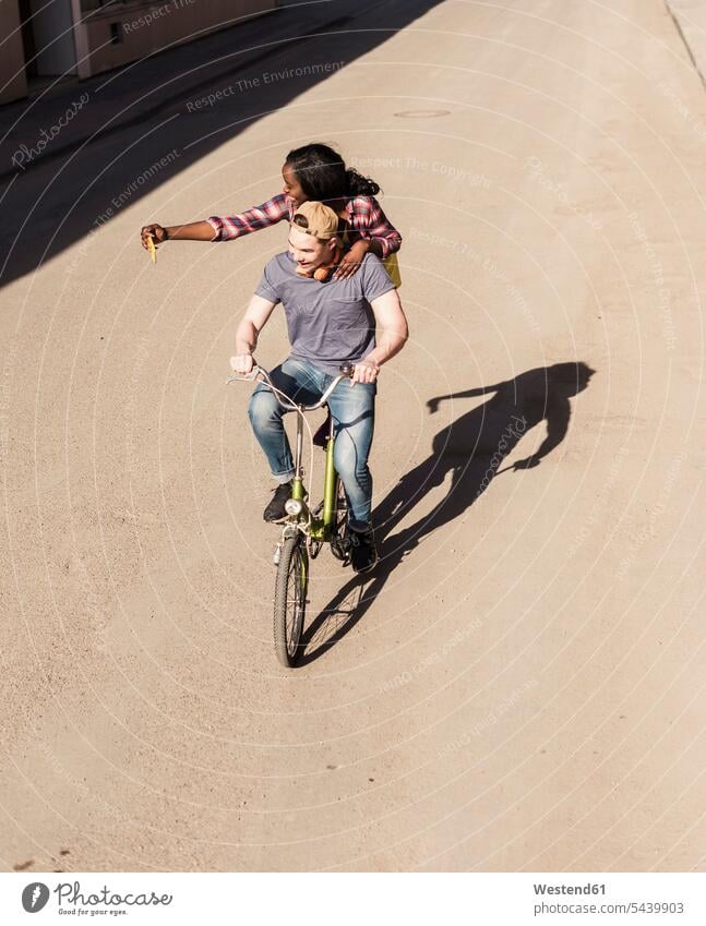 Junger Mann auf dem Fahrrad mit seiner Freundin auf dem Gepäckträger, die Selfies macht radfahren fahrradfahren radeln Bikes Fahrräder Räder Rad jung