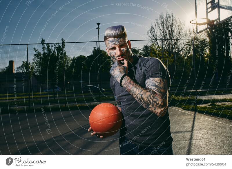 Porträt eines tätowierten jungen Mannes mit Basketball auf dem Platz Sportplatz Sportplaetze Sportplätze Portrait Porträts Portraits Männer männlich Tattoo