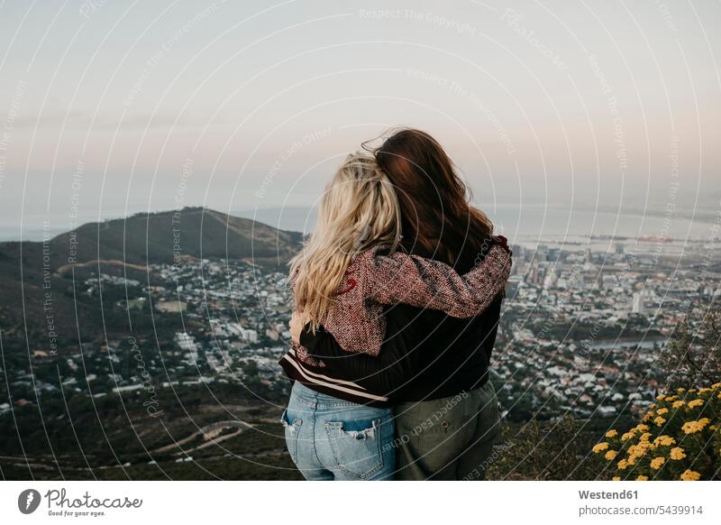 Südafrika, Kapstadt, Kloof Nek, Rückansicht von zwei sich umarmenden Frauen bei Sonnenuntergang Freundin Umarmung Umarmungen Arm umlegen weiblich