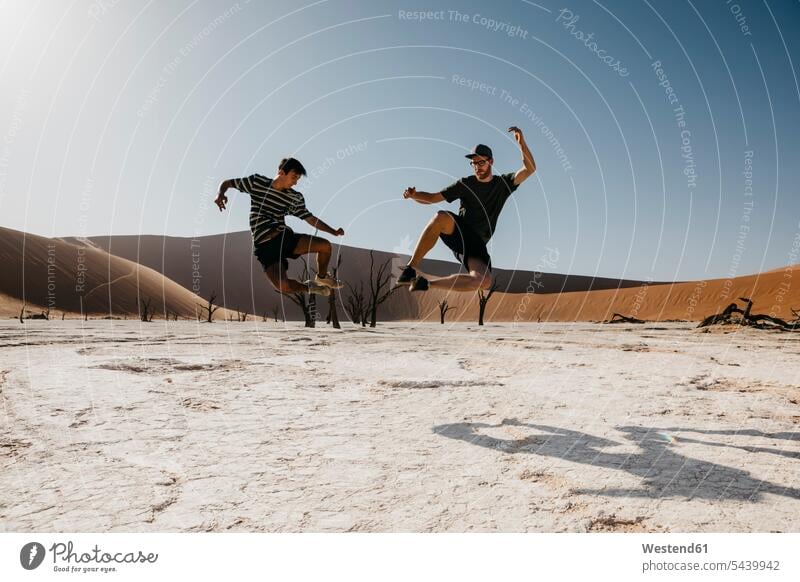 Namibia, Namib-Wüste, Namib-Naukluft-Nationalpark, Sossusvlei, zwei Männer springen im Deadvlei Freunde hüpfen Wüsten Mann männlich Freundschaft Kameradschaft