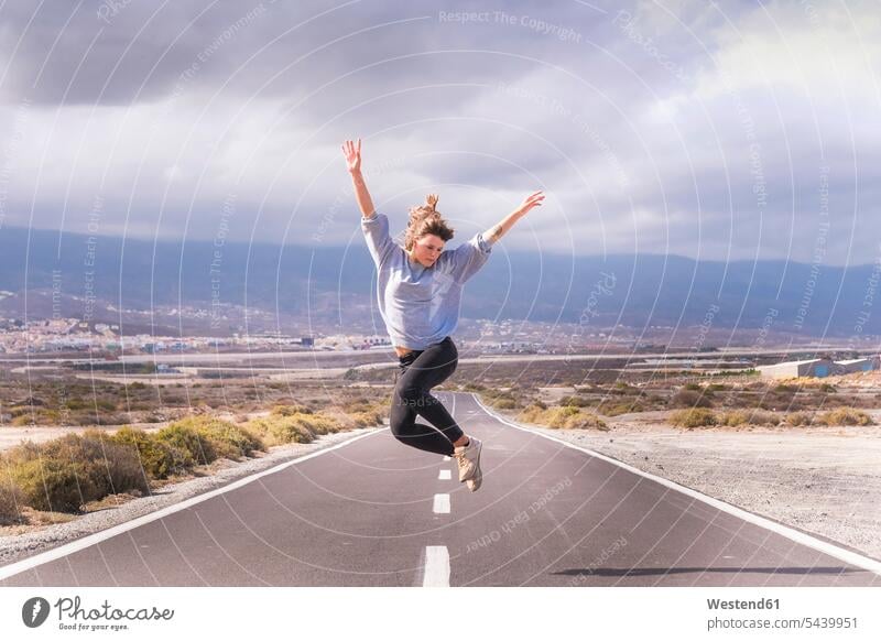 Junge Frau springt vor Freude auf einer Straße weiblich Frauen Strassen Straßen reisen Travel verreisen Weg Reise springen hüpfen Erwachsener erwachsen Mensch