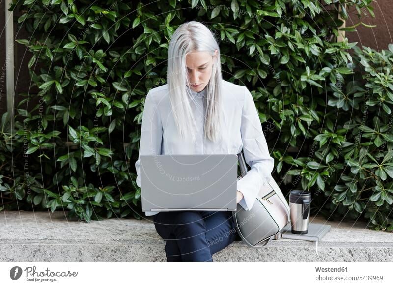 Junge Geschäftsfrau, die in der Stadt mit einem Laptop an einer Wand sitzt Notebook Laptops Notebooks Geschäftsfrauen Businesswomen Businessfrauen Businesswoman