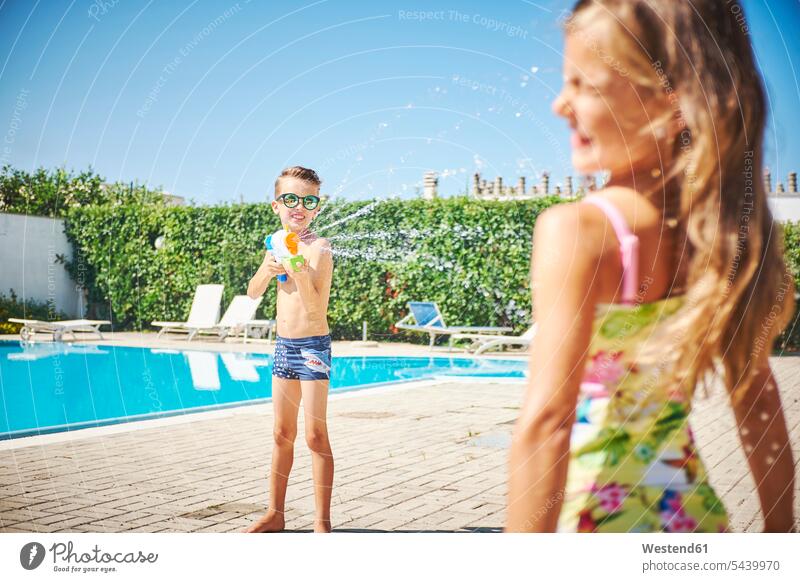 Junge mit Wasserpistole spritzt Mädchen am Beckenrand an Swimmingpool Swimmingpools Schwimmbecken Swimming Pool Swimming Pools weiblich Buben Knabe Jungen