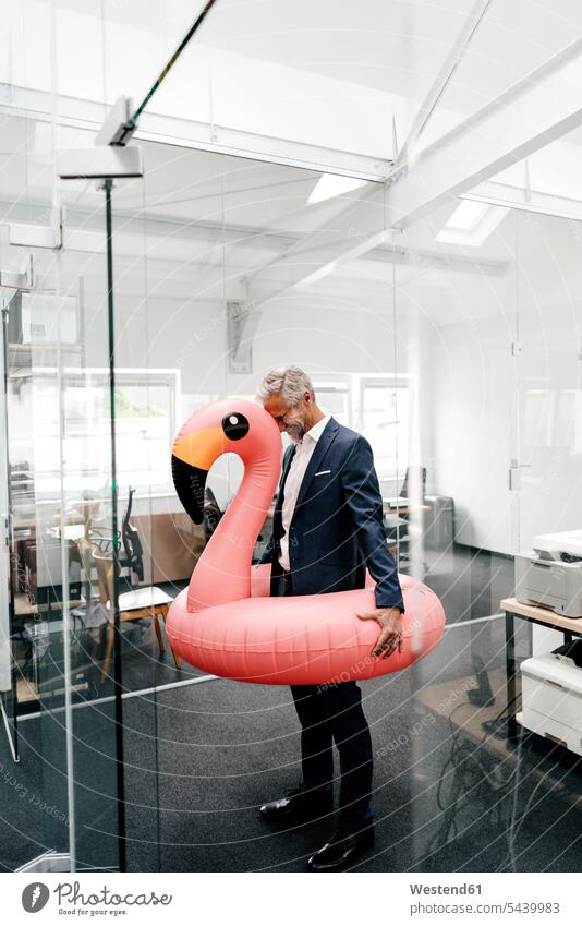 Glücklicher Geschäftsmann im Amt mit aufblasbarem Flamingo Businessmann Businessmänner Geschäftsmänner Büro Office Büros lachen Geschäftsleute Geschäftspersonen