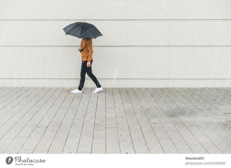 Junger Mann mit Regenschirm geht auf die Straße Leute Menschen People Person Personen Europäisch Kaukasier kaukasisch erwachsen Erwachsene Männer männlich jung