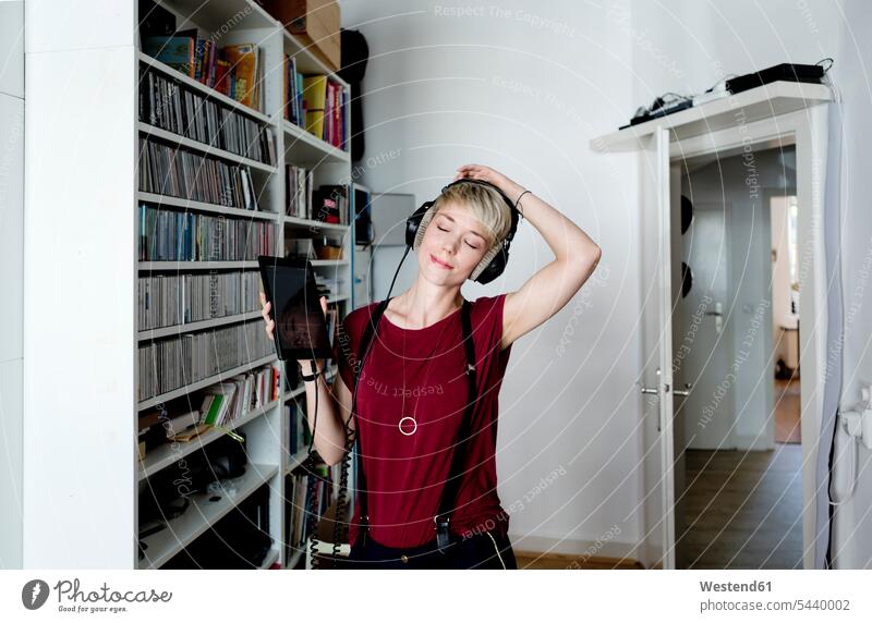 Frau hört Musik mit Kopfhörern zu Hause Deutschland Wohnung wohnen Wohnungen zuhören zuhörend Lifestyle Lebensstil Textfreiraum Freizeitkleidung casual