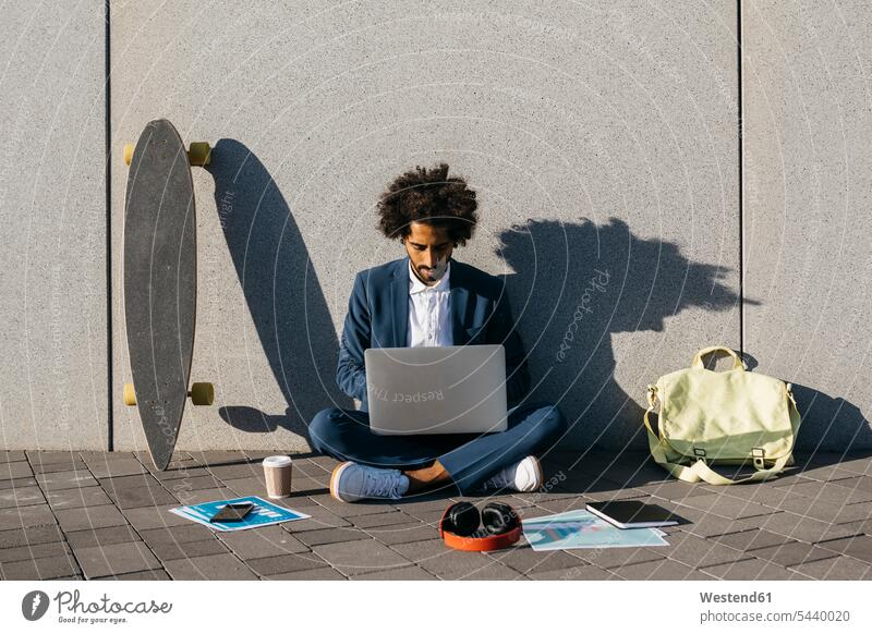 Junger Geschäftsmann sitzt im Freien an einer Wand und arbeitet am Laptop sitzen sitzend Businessmann Businessmänner Geschäftsmänner arbeiten Arbeit Notebook