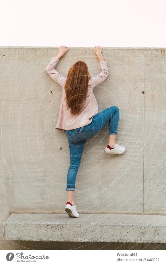 Junge rothaarige Frau klettert auf Betonwand Bänke Sitzbank Sitzbänke steigen abends Erfolge erfolgreich frei Muße kräftig stark Stärke Anreiz Ansporn Antrieb