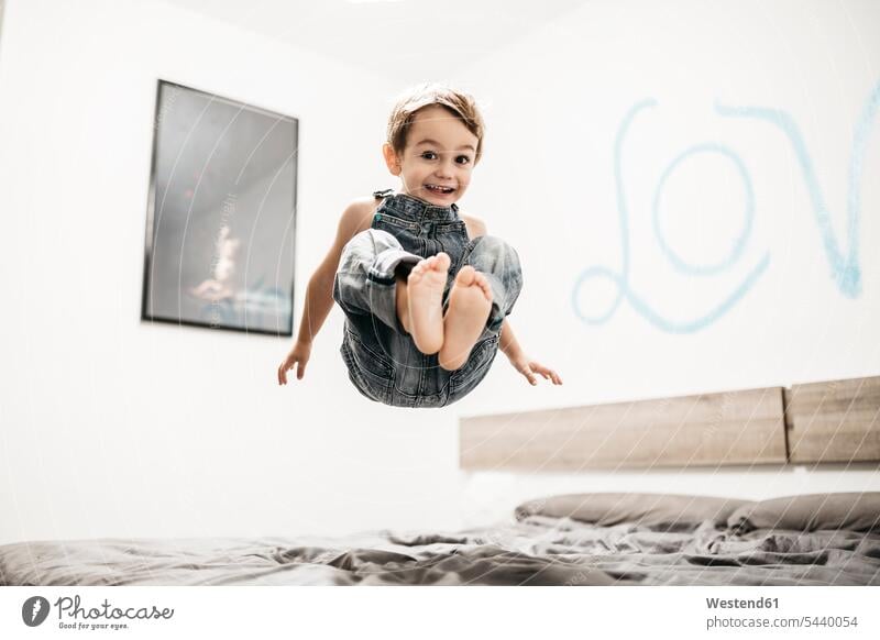 Glücklicher kleiner Junge springt auf dem Bett Luftsprung Luftsprünge einen Luftsprung machen Luftspruenge Betten Buben Knabe Jungen Knaben männlich springen
