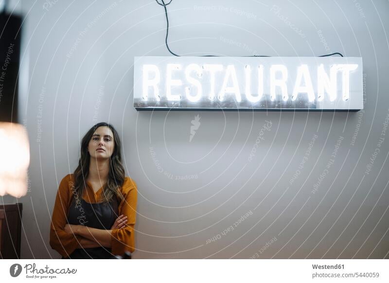 Ernste junge Frau lehnt an einer Wand unter Restaurant Neonlicht Deutschland Selbstständigkeit Selbständigkeit Freiberufler Wort einzelnes Wort