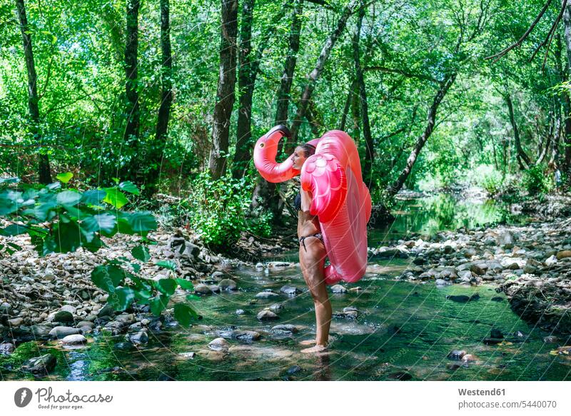 Frau geht im Fluss, trägt einen aufblasbaren Flamingo schwimmen Schwimmsport staunen erstaunen Fluesse Fluß Flüsse stehen stehend steht Sommer Sommerzeit