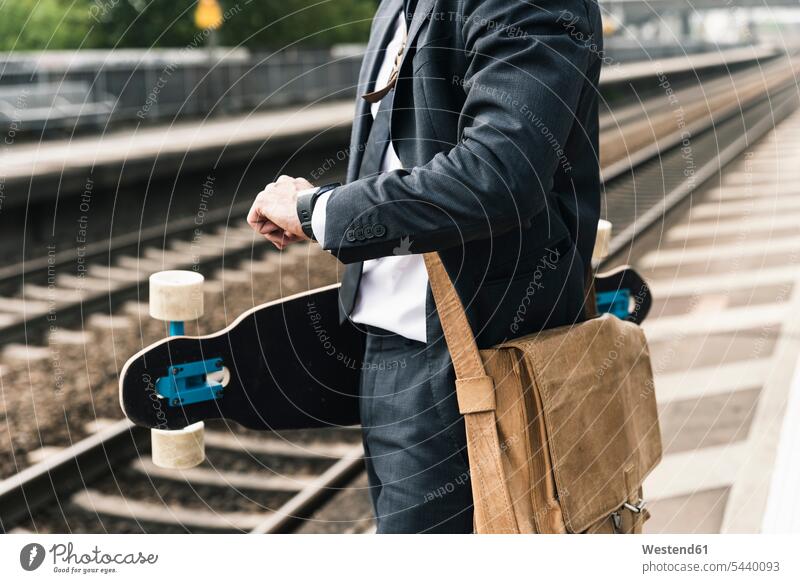 Nahaufnahme eines Geschäftsmannes mit Skateboard, der am Bahnsteig wartet warten Rollbretter Skateboards Zugbahnsteig Zugbahnsteige Bahnsteige Businessmann