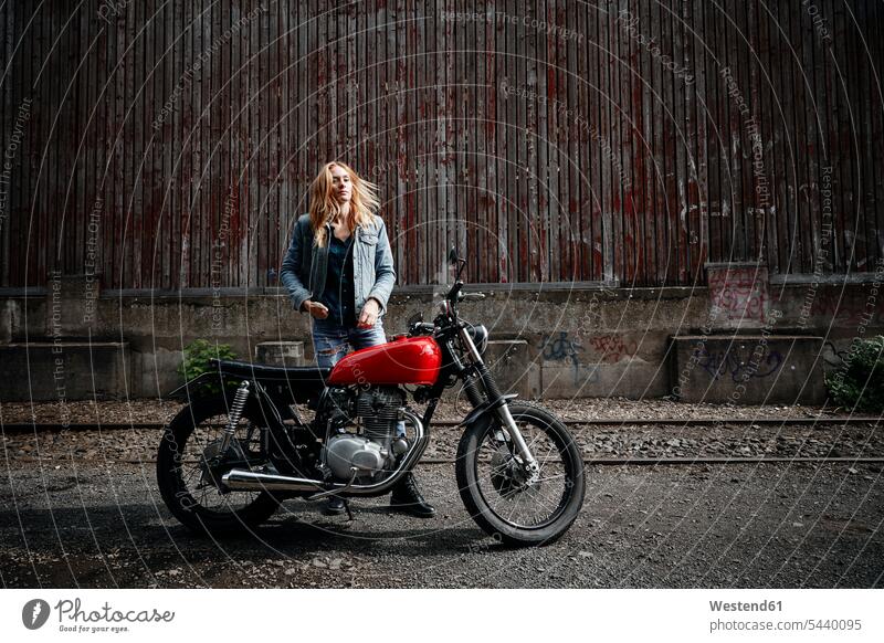 Selbstbewusste junge Frau neben dem Motorrad stehend Motorräder weiblich Frauen steht Zuversicht Zuversichtlich Selbstvertrauen selbstbewusst Vertrauen