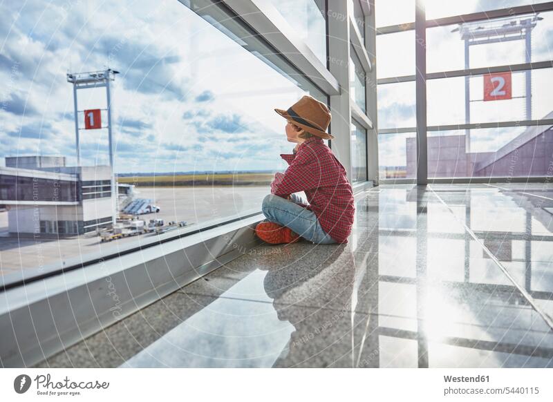 Junge sitzt hinter einer Fensterscheibe am Flughafen und schaut auf das Flugfeld Fensterscheiben Flugfelder Rollfelder Flughaefen Airport Airports Flughäfen