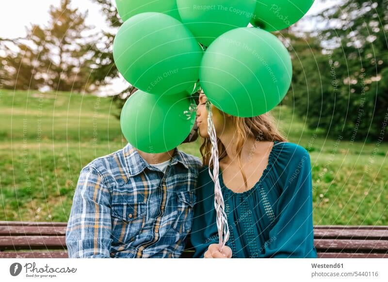 Junges Paar küsst sich hinter grünen Luftballons Ballons Luftballone Pärchen Paare Partnerschaft küssen Küsse Kuss Mensch Menschen Leute People Personen