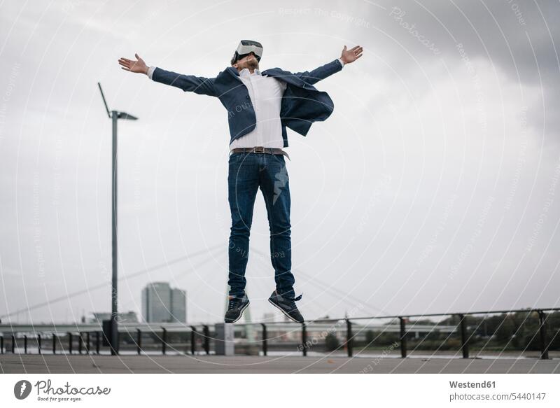 Geschäftsmann mit VR-Brille springt in der Stadt staedtisch städtisch Virtuelle Realität Virtuelle Realitaet Brillen Businessmann Businessmänner Geschäftsmänner