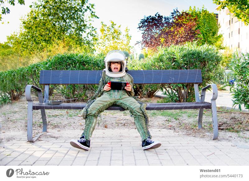 Junge in Raumanzug und auf einer Bank sitzend, mit Tablette Leute Menschen People Person Personen Europäisch Kaukasier kaukasisch 1 Ein ein Mensch