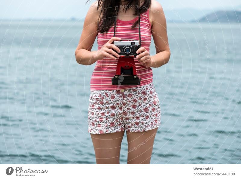 Griechenland, Amfilochia, Frau mit Oldtimer-Kamera am Meer Meere weiblich Frauen Küste Küstenlandschaft Fotoapparat Fotokamera Gewässer Wasser Erwachsener