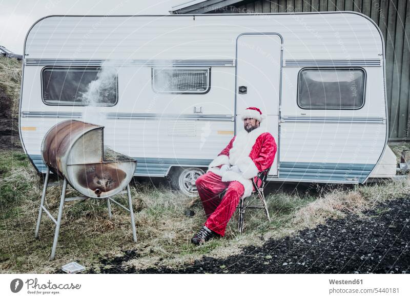 Island, Weihnachtsmann sitzt vor Wohnwagen und grillt Weihnachtsmänner Weihnachtsmaenner Santa Claus Nikolaus Campingwagen Caravan grillen sitzen sitzend