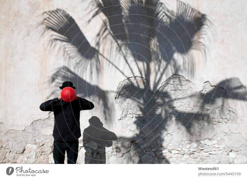 Marokko, Essaouira, Mann mit Melone, der einen roten Luftballon vor seinem Gesicht an einer Wand hält roter rotes Bowlerhut Bowler Hat Männer männlich halten