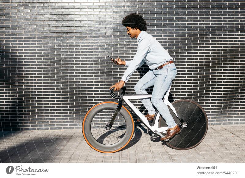 Mittelgroßer erwachsener Mann fährt mit dem Fahrrad, benutzt Smartphone Mann mittleren Alters Männer mittleren Alters Bikes Fahrräder Räder Rad simsen lesen