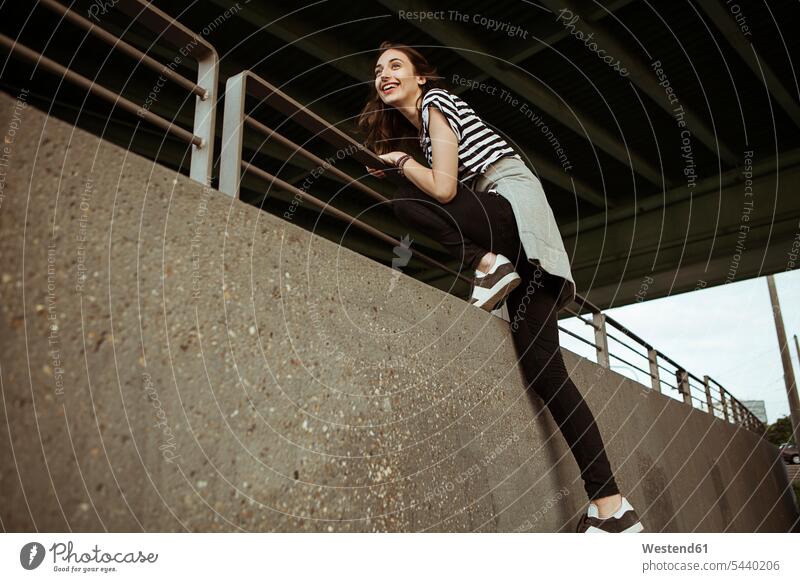 Glückliche junge Frau auf Geländer unter einer Brücke lachen weiblich Frauen positiv Emotion Gefühl Empfindung Emotionen Gefühle fühlen Empfindungen emotional