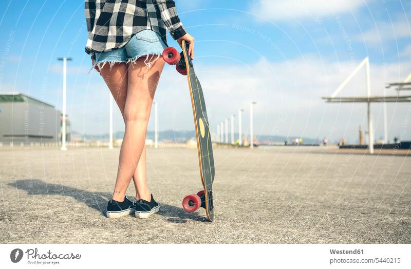 Rückenansicht einer jungen Frau mit Longboard vor der Strandpromenade, Teilansicht weiblich Frauen Skateboarderin Skateboardfahrerin Skaterin Skateboarderinnen