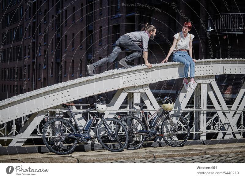 Deutschland, Hamburg, Ehepaar mit Elektrofahrrädern beim Spaß auf einer Brücke Paar Pärchen Paare Partnerschaft E-Bike eBikes E-Bikes Elektrofahrrad Elektrorad