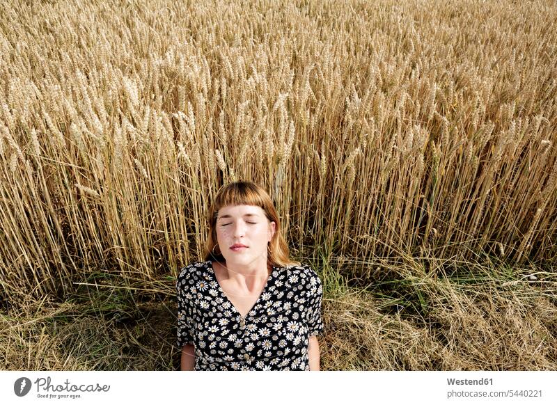 Porträt einer jungen Frau mit geschlossenen Augen, die sich vor einem Getreidefeld entspannt Leute Menschen People Person Personen 1 Ein ein Mensch