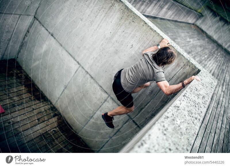 Sportler klettert Betonwand im Freien hoch Betonwände Betonwaende klettern steigen Mann Männer männlich Wand Wände Waende Erwachsener erwachsen Mensch Menschen
