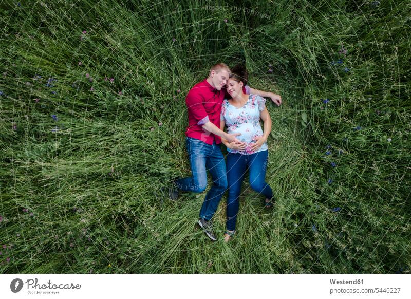 Schwangere Frau und Mann halten Babybauch, liegen auf der Wiese anfassen Berührung behüten behütet geborgen Sicherheit Glück glücklich sein glücklichsein