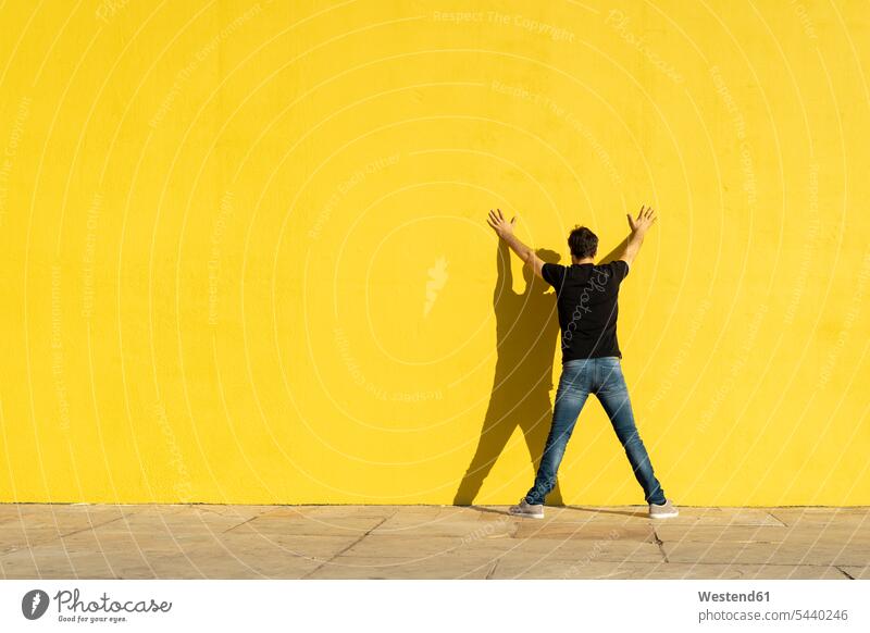 Mann stehend mit Händen an gelber Wand, Rückansicht anlehnen angelehnt lehnend Mauer Mauern gelbes steht Männer männlich Rueckansicht Rückenansicht