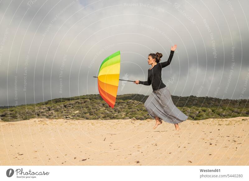 Frau hält bunten Regenschirm auf einer Düne weiblich Frauen kämpfen kaempfen Sonnenschirm Sonnenschirme unangepasst Unangepasstheit Stranddüne Strandduene