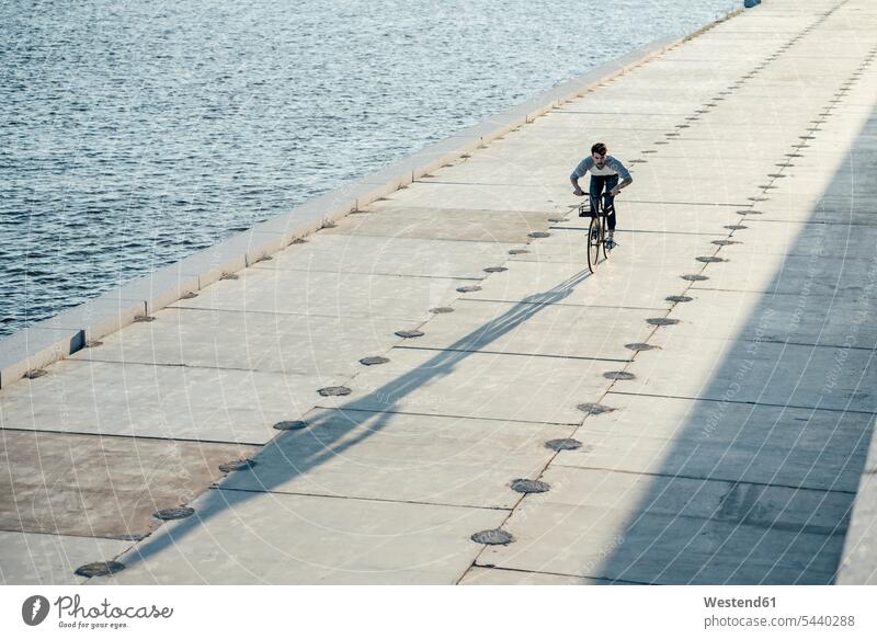 Junger Mann fährt Fahrrad auf der Uferpromenade am Flussufer Bikes Fahrräder Räder Rad Uferpromenaden Fluesse Fluß Flüsse Männer männlich fahren Raeder
