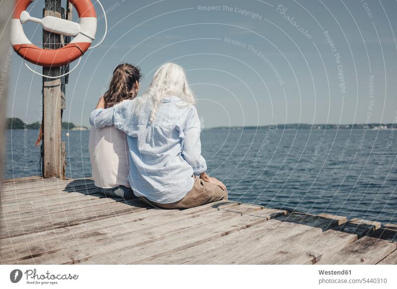 Mutter und Tochter schauen auf das Meer, auf dem Steg sitzend, Rückansicht Leute Menschen People Person Personen Europäisch Kaukasier kaukasisch 2 2 Menschen