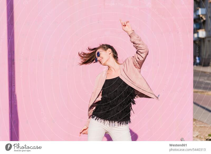 Glückliche junge Frau, die sich vor einer rosa Wand bewegt Wände Waende glücklich glücklich sein glücklichsein rosafarben bewegen weiblich Frauen Farbe Farbtöne