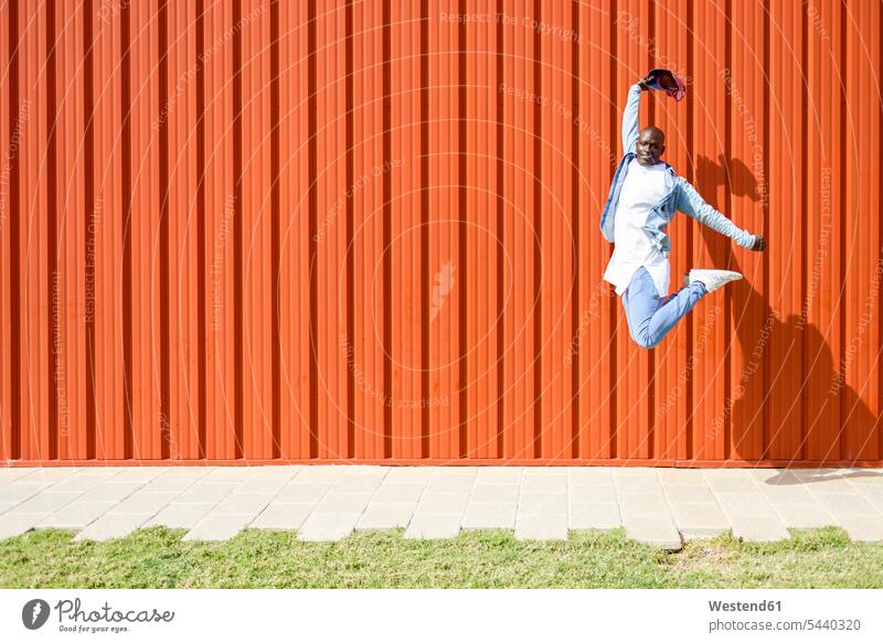 Mann in lässiger Denim-Kleidung springt in die Luft vor einer orangefarbenen Wand Jeans Jeanshose Luftsprung Luftsprünge einen Luftsprung machen Luftspruenge